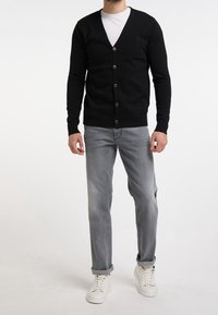 Cardigan nero in maglia con scollo a V, chiusura a bottoni, polsini e orlo a costine, abbinato a jeans grigi chiari e sneakers bianche.