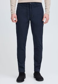 Temno modre raztegljive hlače z vrvico na pasu, slim fit slog in mehak teksturiran material. Primerne za vsakodnevno nošenje.
