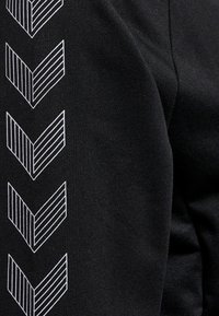 Svart tyg med en texturerad yta som har ett upprepat vitt geometriskt chevronmönster längs ena sidan.