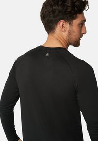 Schwarzes langärmliges Sportshirt mit Rundhalsausschnitt, strukturiertem Stoff und Raglanärmeln. Subtile Logodetails in der Nähe des Rücken-Halsausschnitts.