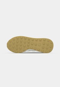 Hvit sneaker såle med en teksturert, gul gummi bunn som har rektangulære nagler og en avrundet form. Ren, minimalistisk design med lette kurver.