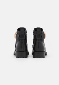 Botas de cuero negras hasta el tobillo con un diseño elegante, que cuentan con una correa decorativa y un acento de hebilla, suelas robustas y detalles de costura mínimos.