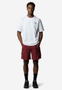 Hvid kortærmet t-shirt med sort logo, parret med røde cargo shorts med sidelommer og en sort bæltestrop, båret med sorte sneakers.