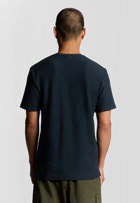 Marineblauwe t-shirt met korte mouwen, gemaakt van textuurstof, met een ronde hals en een ontspannen pasvorm, gezien vanuit de achterkant.