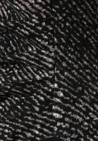 Tissu noir et beige à motifs affichant un tissage texturé. Présente des détails de fronces légères et une texture douce et duveteuse sur l'ensemble.