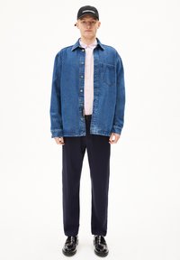 Blauwe denimshirt met knoopsluiting, roze overhemd met kraag eronder, marineblauwe broek, zwarte pet en zwarte schoenen. Eenvoudig ontwerp met een zakdetail.