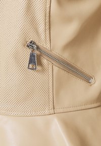 Tejido de cuero beige con sección perforada y cremallera diagonal plateada, resaltando detalles de textura y costuras.