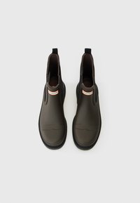Bottes en caoutchouc marron jusqu'à la cheville avec des panneaux élastiques sur les côtés, dessus texturé, semelles noires et un petit logo rouge et blanc à l'avant.