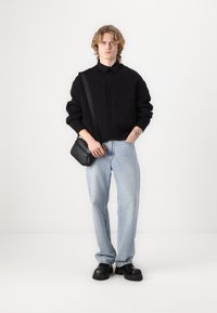 Cardigan de malha preta com botões, combinado com jeans de perna reta azul claro e sapatos pretos de sola grossa. Pequena mala preta de ombro com alça.