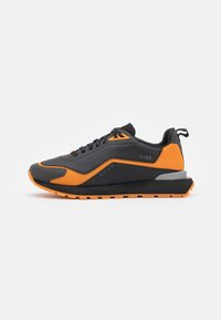 Scarpe da ginnastica nere e arancioni con una superficie testurizzata, design con lacci e una suola spessa con un tallone grigio accentuato.