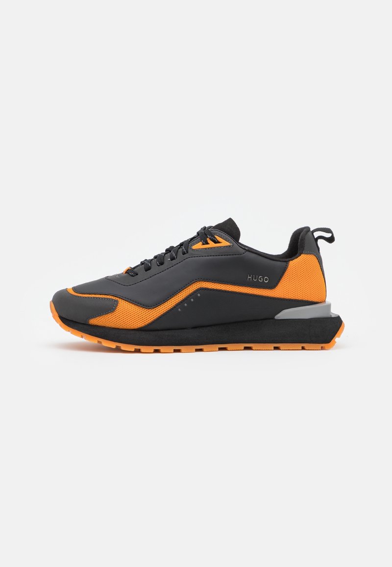 Scarpe da ginnastica nere e arancioni con una superficie testurizzata, design con lacci e una suola spessa con un tallone grigio accentuato.