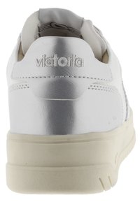 Sneaker bianco con tomaia in pelle liscia, tacco piatto e accenti argentati a contrasto. Presenta dettagli cuciti e un colletto imbottito.
