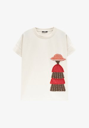 Biały t-shirt z krótkim rękawem z dekoracyjnym wzorem kobiety noszącej czerwony i pasiasty kapelusz oraz wielowarstwową czerwoną i brązową sukienkę z koralików.