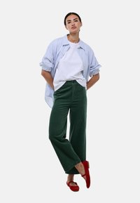 Pantalons en velours côtelé verts à jambes larges, t-shirt blanc et chemise oversize à rayures bleues et blanches. Ballerines rouges avec un accent en nœud.