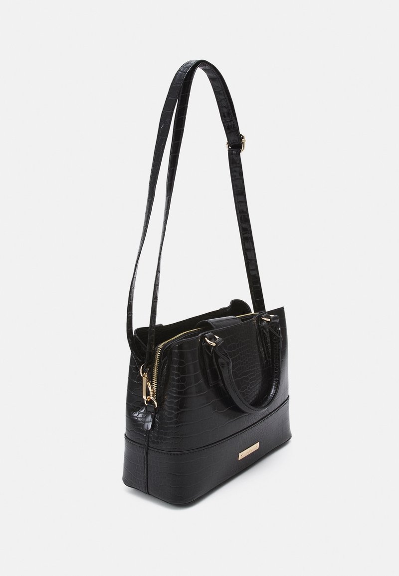 Sac à main noir avec texture crocodile, fermeture éclair dorée, poignées courtes et longue bandoulière réglable sur fond blanc.