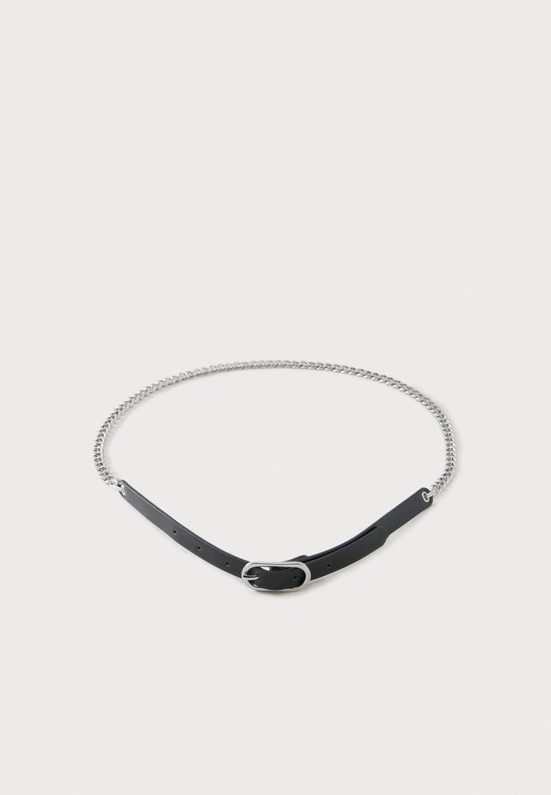 Ceinture en cuir noir et chaîne argentée avec boucle, disposée en cercle sur un fond blanc uni.