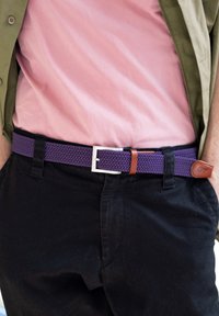 Lila geflochtenem Gürtel mit silberner Metallschnalle und einem braunen Lederakzent. Kombiniert mit einem pinken T-Shirt und schwarzen Hosen, zeigt einen lässigen Stil.