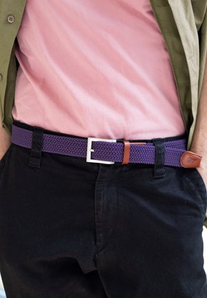 Cintura intrecciata viola con fibbia in metallo argentato e un accento in pelle marrone. Abbinata a una maglietta rosa e pantaloni neri, mostra uno stile casual.