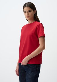 T-shirt rosso a maniche corte in cotone con scollatura rotonda. Presenta una vestibilità comoda e una texture liscia. Abbinato a jeans in denim scuro.
