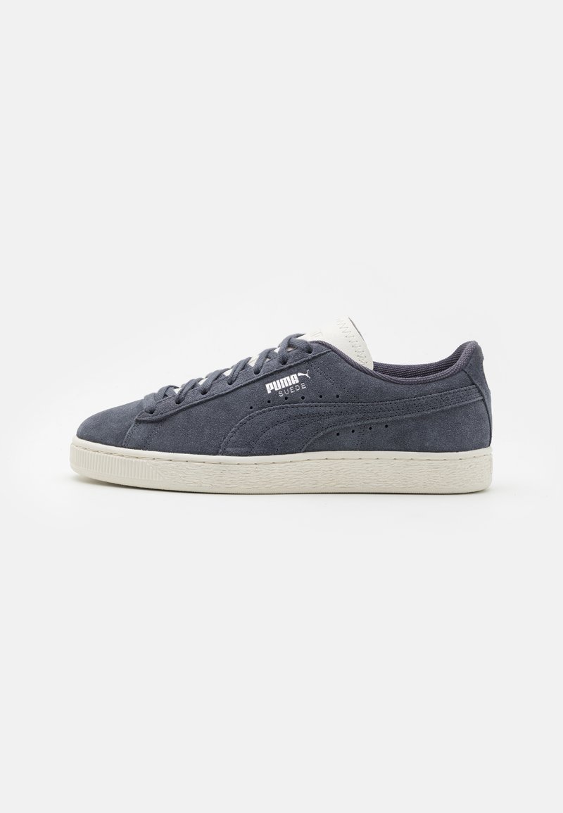 Grey suede sneakers with cream rubber sole, featuring a padded collar, white logo, and perforated accents on the side. Laced design.