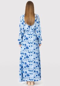 Lang blå blomstret kjole med en lyseblå baggrund og mørkeblå blomstermønstre, lange ærmer og en indsnævret talje for form.
