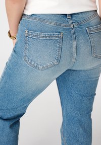 Lichtblauwe denim jeans met een relaxte pasvorm, voorzien van twee achterzakken en zichtbare stiksels langs de naden. Zachte, gestructureerde stof.