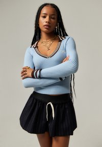 Hellblauem geripptes Sweatshirt mit V-Ausschnitt und braunen Akzenten. Kombiniert mit einem schwarzen gestreiften Rockshort mit einer Zugbandtaille.