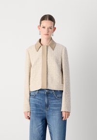 Beige Cropped-Jacke mit einer Tweed-Textur, einem braunen Kragen und Verschluss vorne. Kombiniert mit blauen hoch taillierten Jeans.