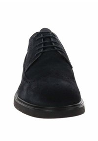 Chaussure en daim noir avec un bout arrondi, dotée de lacets et de perforations décoratives. La semelle est plate et faite d'un matériau durable.