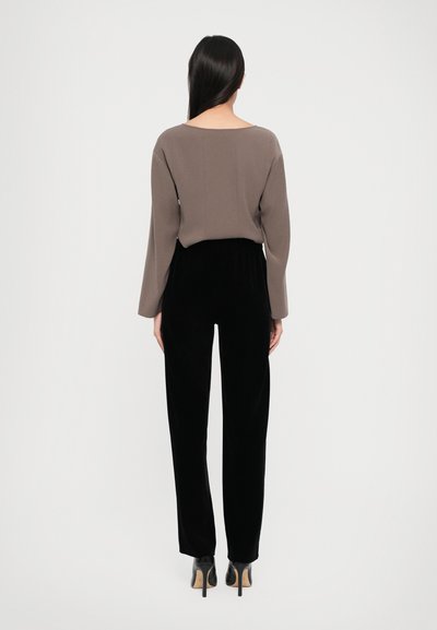 Haut marron à manches longues avec un col large, associé à un pantalon en velours noir. L'ensemble présente une coupe décontractée et une longueur à la cheville.