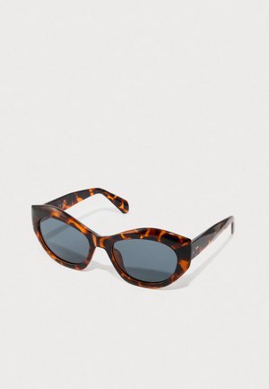 Mačke sunčane naočale u boji kornjače s tamnim lećama, odložene na jednostavnoj svijetloj površini.