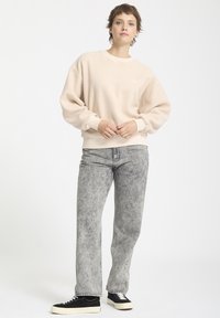 Sweter z kremowego polaru z okrągłym dekoltem i opadającymi szwami na ramionach, w połączeniu z szarymi dżinsami i czarnymi trampkami.
