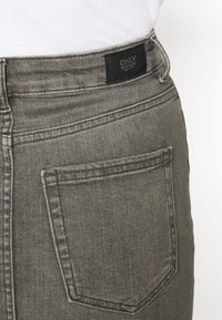 Jeans de mezclilla gris de tiro alto, con una etiqueta negra en la parte posterior y un diseño de bolsillo estándar con detalles de costura visibles.