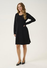 Abito lungo nero a maniche lunghe con scollo a barchetta e gonna svasata. Realizzato in tessuto morbido, presenta un design semplice senza motivi o accenti.