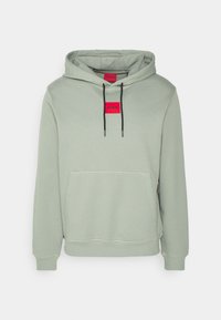 Felpa verde chiaro con tasca frontale, cappuccio regolabile con cordino e un'etichetta rossa rettangolare. Polsini e orlo a coste. Materiale morbido.