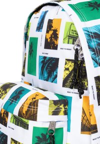 Ryggsäck med ett vitt tyg som har flerfärgade fototryck av palmträd och urbana scener. Inkluderar dubbla dragkedjor och en framficka.