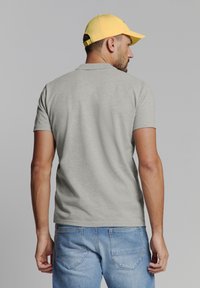 Grijze korte mouwen T-shirt van katoen, met een ronde halslijn. Gemaakt in combinatie met lichtblauwe spijkerbroek en een gele pet.