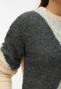 Kootud kampsun halli ja kreemika värvi plokkidega, millel on pehme tekstuur, sooniline kaelus ja lühikesed varrukad kontrastsete detailidega.