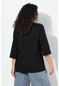 Zwarte top met driekwart mouwen en een ontspannen pasvorm; zachte, lichte stof; gecombineerd met lichtblauwe denim jeans met hoge taille.