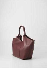 Burgunderfarget, teksturert syntetisk totebag med to hendlene, en frontlomme og glidelås lukking på toppen. Rund form med vid åpning.