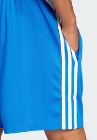 Shorts de sport bleus avec des rayures blanches sur les côtés, en matériau léger, avec des poches et une texture lisse.