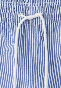 Blau-weiß gestreifter Stoff mit weißen vertikalen Streifen, mit einem weißen Kordelzug, der durch Metallösen an einem elastischen Bund geführt wird.