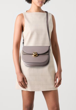 Gray leather shoulder bag with a curved flap, gold hardware detail, and adjustable strap, paired with a light plaid dress.