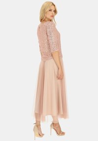 Złoty top cekinowy w kolorze różowego złota z rękawami 3/4, zestawiony z miękką, zwiewną spódnicą z tiulu w delikatnym różowym kolorze oraz cielistymi sandałami na obcasie.