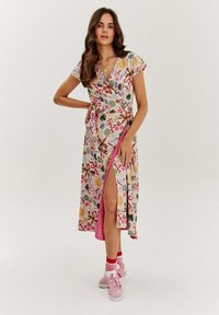 Květinové šaty s volnými rukávy v pastelových barvách, s vysokým rozparkem a růžovou podšívkou. Kombinované s růžovými teniskami a červenými kotníkovými ponožkami.