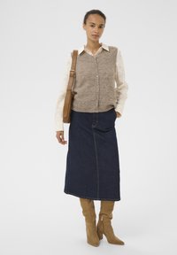 Strikket beige cardigan over en cremefarvet skjorte med teksturerede ærmer, parret med en mørk denimnederdel og brune knæhøje støvler.