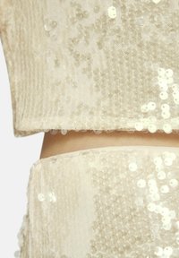 Beige pailletten top met een doorschijnende basis. Heeft een cropped ontwerp en een delicate zoom. De pailletten zijn gelijkmatig en weerkaatsen het licht.