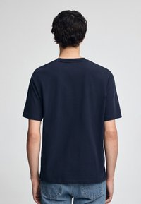 Camiseta de algodón azul marino con mangas cortas y cuello redondo, que presenta un diseño trasero limpio sin logotipos ni patrones visibles.