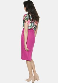 Jasnoróżowa spódnica ołówkowa z wysokim stanem i rozporkiem z tyłu, zestawiona z kwiecistą bluzką z krótkim rękawem w różnych kolorach i wzorach.