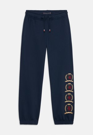 Navyblaue Sweatpants mit elastischem Bund und Kordelzug. Mit vier gestickten Wappenmotiven in Rot und Gold entlang des Beins.
